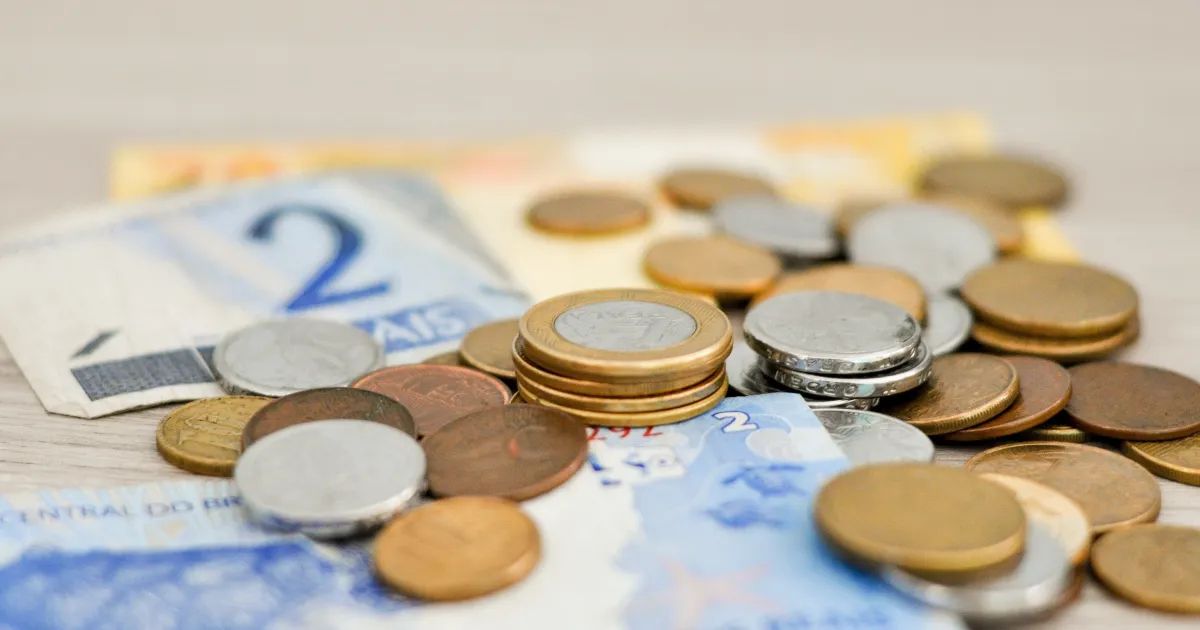 Mãos segurando moedas e notas sobre mesa