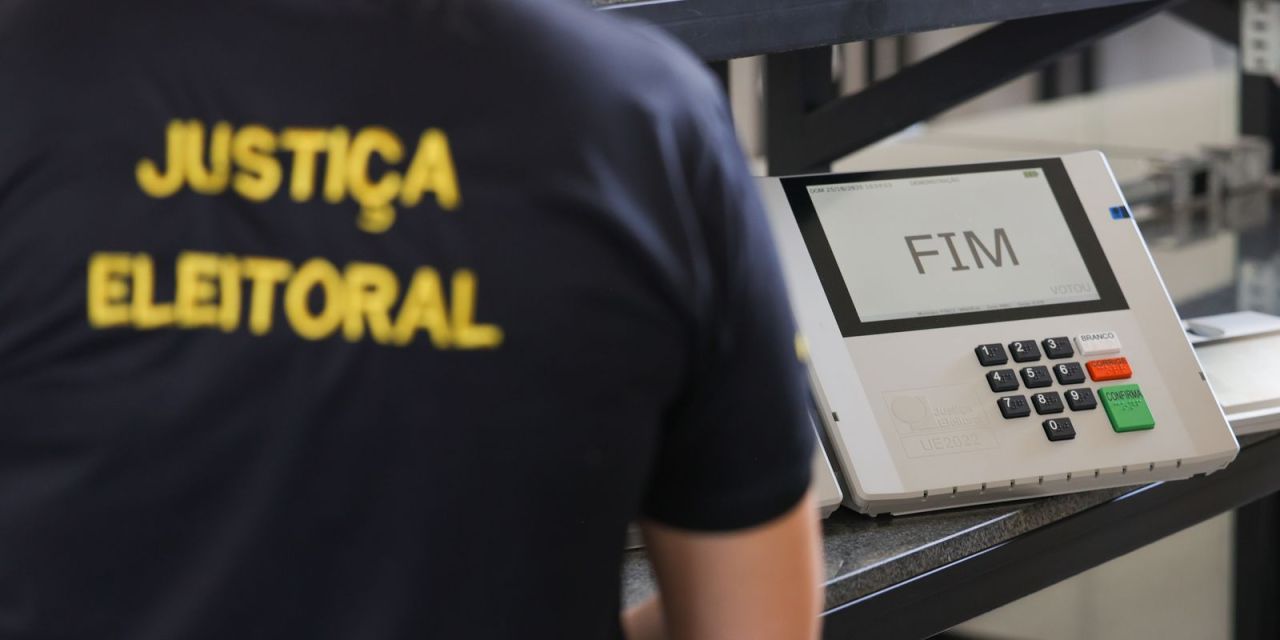 Trabalhador segurando carteira de trabalho ao lado de urna