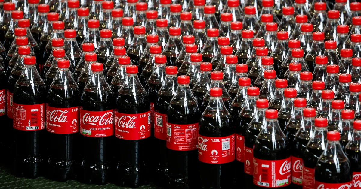 Garrafas e latas de refrigerante Coca-Cola em prateleira de supermercado