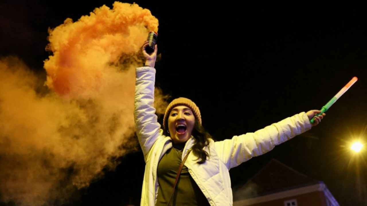 Multidão comemorando em Budapeste com a Ponte das Correntes iluminada nas cores da bandeira húngara