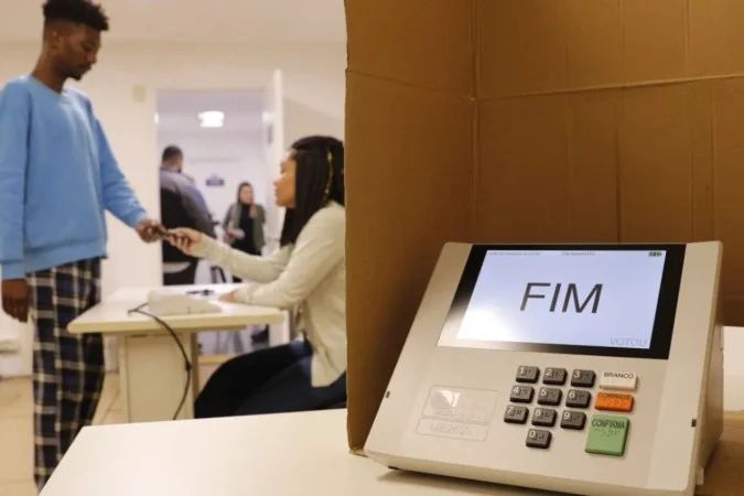 mesários trabalhando com urna eletrônica em seção eleitoral