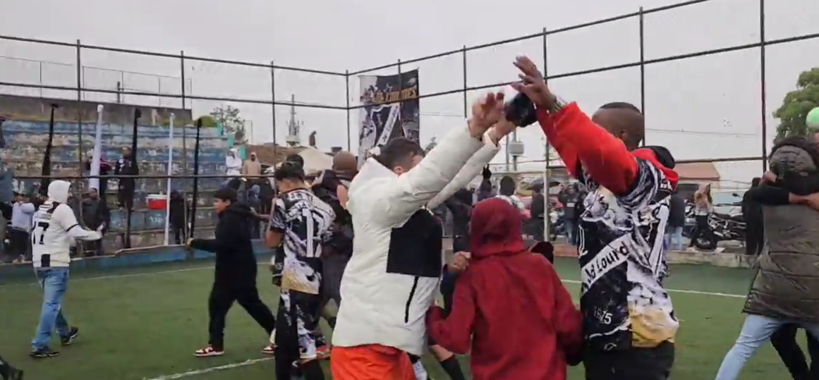 Final da Copa Jardim do Sol entre Jardim Lourdes e Leão do Norte em campo lotado com torcida animada, decisão nos pênaltis sob chuva e frio.