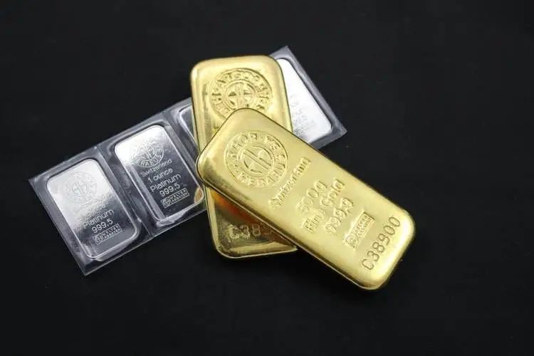 Barras e moedas de ouro e prata sobre superfície escura