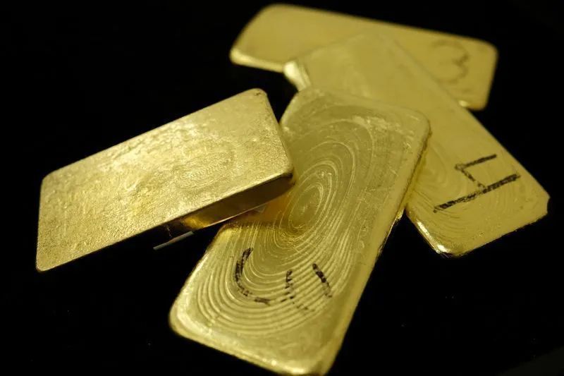 Barras de ouro sobre mesa com gráfico de mercado ao fundo