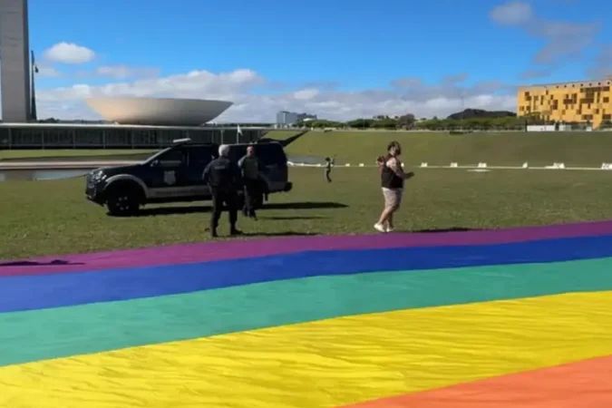 Ativistas com bandeira LGBTQIAPN+ no gramado em frente ao Congresso Nacional
