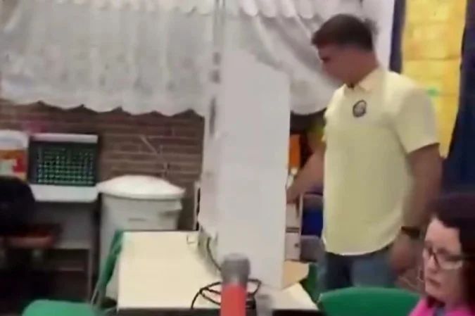 Mesária com expressão séria ao receber Flávio Bolsonaro na seção de votação