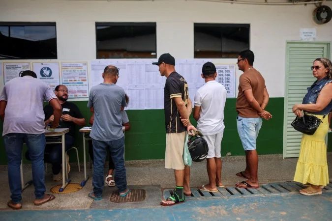 Urna eletrônica e mesários em local de votação